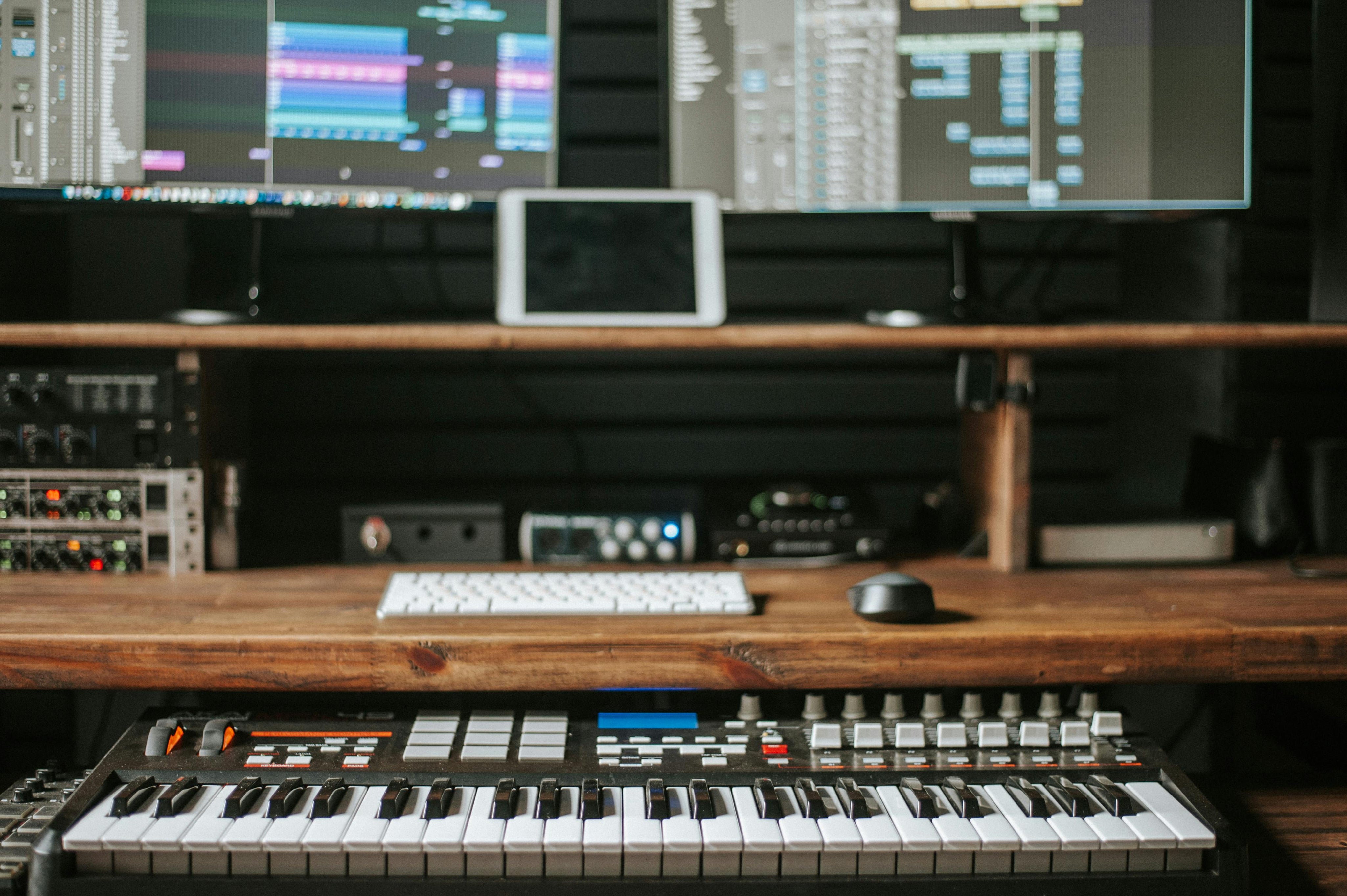 Music production setup with keyboard, monitors, and equipment on a wooden desk.